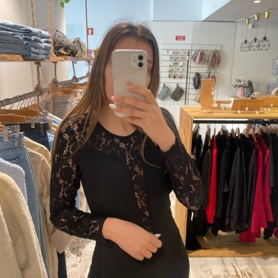 Mulher com blusa preta de renda a tirar selfie numa loja de roupa com cabides e roupas ao fundo