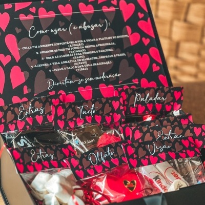 Caixa preta aberta com pacotes decorados com corações e etiquetas com nomes dos sentidos.