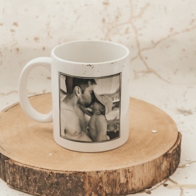 Caneca branca com fotografia a preto e branco de um homem e uma criança, em cima de base de madeira