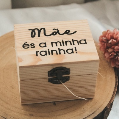 Caixa de madeira clara gravada com texto sobre tronco de madeira e flores cor de rosa