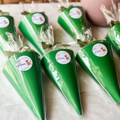 Cones verdes embalados com laço e etiqueta comemorativa Liam colocados sobre superfície branca.