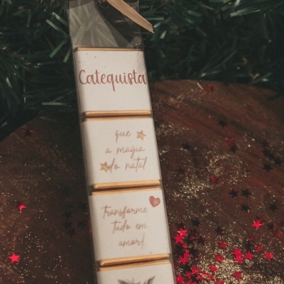 Barras de chocolate empilhadas com embalagem branca e texto em português sobre tecido castanho com glitter e confetes vermelhos em formato de estrela.