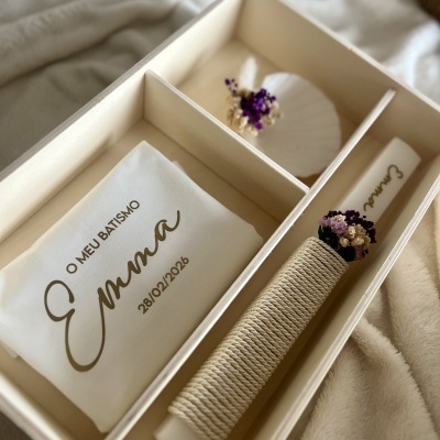 Kit batismo com vela decorada, toalha branca com texto e concha com flores secas em caixa de madeira.