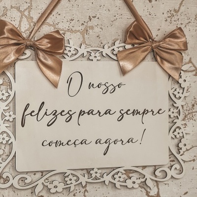 Placa decorativa creme com moldura floral e laços dourados, texto em português, pendurada na parede