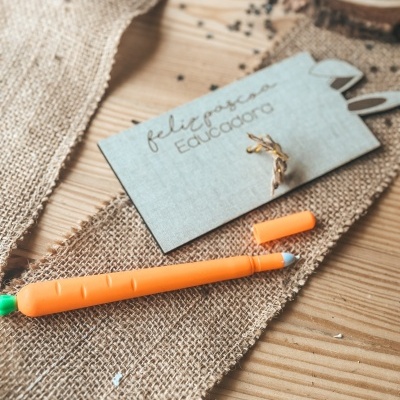 Caneta laranja em forma de cenoura com tampa ao lado e cartão cinza com texto