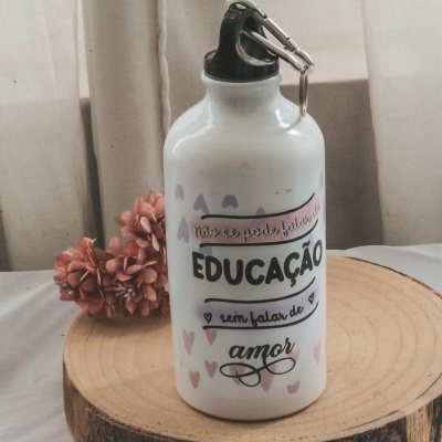 Garrafa branca de alumínio com texto em português sobre base de madeira e flores ao fundo