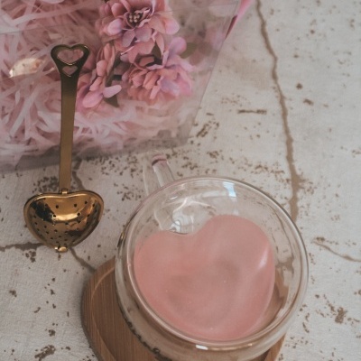 Colher de chá dourada em forma de coração, flores cor de rosa, chávena de vidro com interior cor de rosa em forma de coração, base de madeira em forma de coração