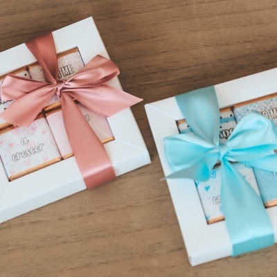 Duas caixas de presente brancas com fitas rosa e azul sobre madeira clara