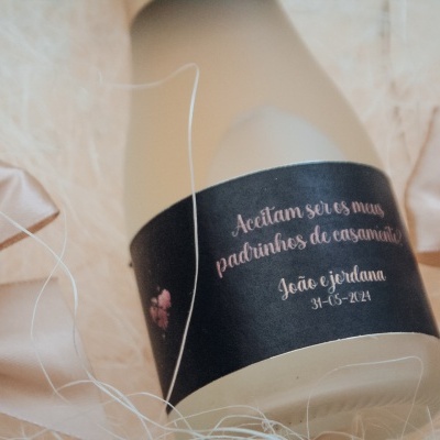 Frasco com etiqueta preta e texto branco sobre tecido bege claro com laços de cetim.