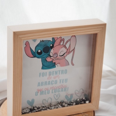 Quadro de madeira com ilustração de Stitch e Angel abraçados e texto em português, sobre uma base de madeira rústica com confetes.