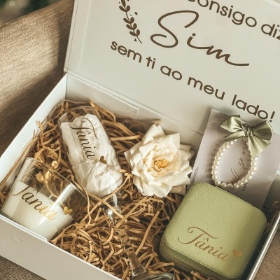 Caixa de presente branca com copo, vela, taça, saco, flor artificial, caixa verde e pulseira de pérolas.