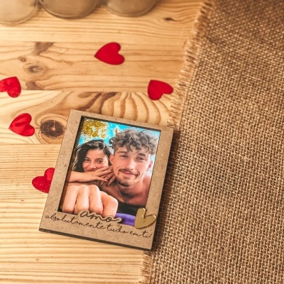 Moldura de madeira com foto de casal e texto gravado, sobre mesa de madeira e tecido de juta com corações vermelhos