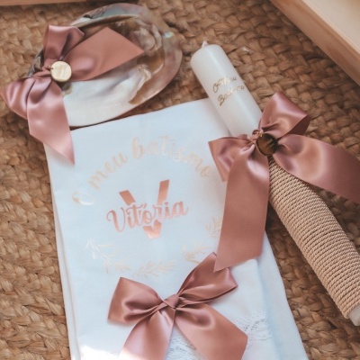 Conjunto de vela, toalha e laços rosas para batizado sobre superfície rattan