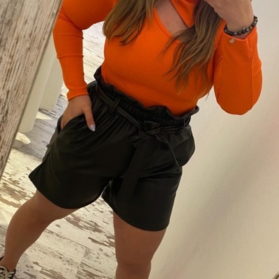 Mulher com camisa laranja e calções pretos tira selfie em espelho