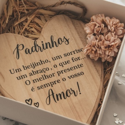 Placa decorativa de madeira em forma de coração com texto em português, em caixa branca e flores cor de rosa.