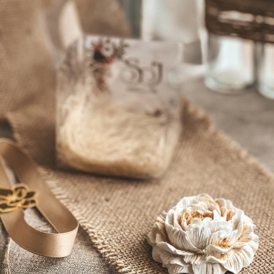 Flor decorativa branca sobre tecido de juta com fita bege ao lado
