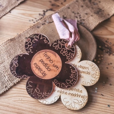 Pendentes florais em acrílico castanho e madeira clara com mensagens gravadas, sobre mesa de madeira e tecido rústico.