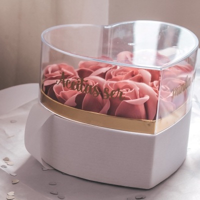 Caixa transparente com flores cor-de-rosa e base dourada numa tampa branca
