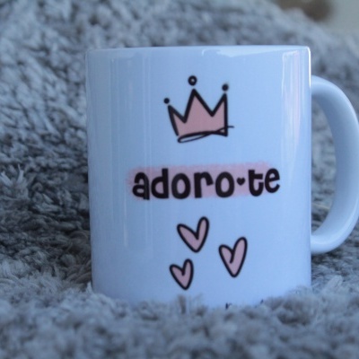 Caneca branca com mensagem 'adoro-te', coroa e corações cor-de-rosa sobre cobertor cinzento