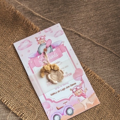 Convite de batizado rosa com ilustrações infantis e flores secas sobre tecido de juta e mesa castanha