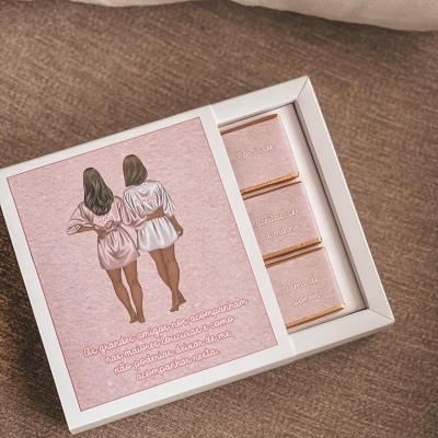 Caixa branca com chocolates decorados e tampa com ilustração de duas mulheres e texto em português