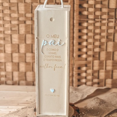 Caixa de madeira clara para garrafa com texto em português sobre mesa de madeira e parede entrelaçada ao fundo.