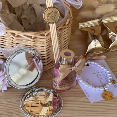 conjunto de produtos com cesto de vime, espelho, frasco com laço, pulseira, embalagens douradas e plantas secas