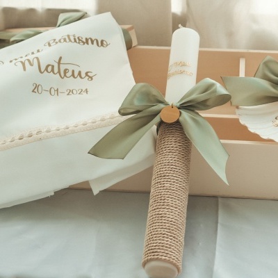 Conjunto de batismo com toalha, vela e sabão decorado, tudo numa caixa de presente sobre mesa branca.