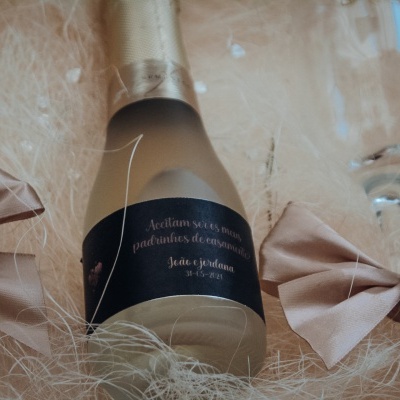 Garrafa decorativa com etiqueta preta, laços rosas e luzes LED numa base de fibras claras