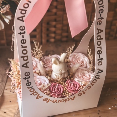 Arranjo decorativo com flores artificiais e figura de coelho em caixa com laço rosa