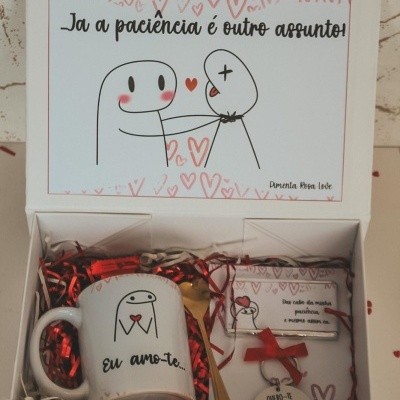 Caixa de presente branca com caneca, colher dourada, barra de chocolate e pendente, decoração com corações e texto em português.