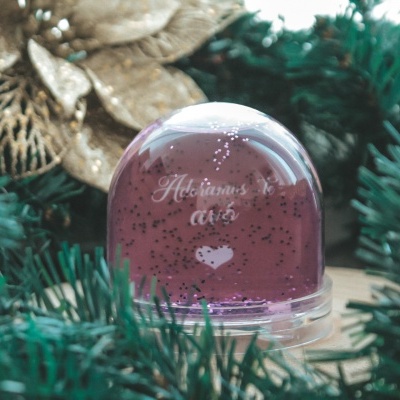 Globo de neve com texto branco e decoração de pinheiro e ornamentos dourados