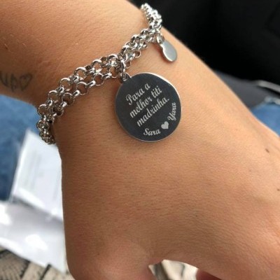 Pulseira metálica prateada com pendente redondo gravado no pulso