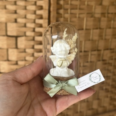 Pequena figura de anjo branca dentro de redoma de vidro com etiqueta e fita verde