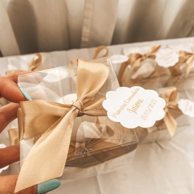 Caixa de presente transparente com laço dourado e etiqueta personalizada em fundo claro
