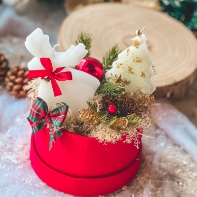 Arranjo decorativo de Natal com vela em forma de rena e árvore, pinhas e folhas verdes num recipiente vermelho