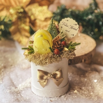 Arranjo natalício decorativo com vela amarela e laço dourado numa base branca