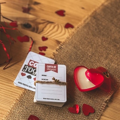 Cartas de jogo e cartas de desejo empilhadas com corda e confetes em forma de corações vermelhos numa mesa de madeira com vela de coração.