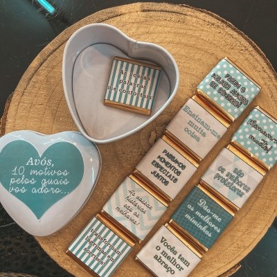 Caixa em forma de coração com chocolates decorados com frases para avós sobre uma base de madeira redonda