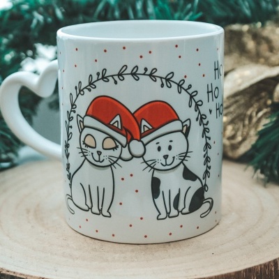 Caneca de cerâmica branca com desenhos de dois gatos com gorros de Natal vermelhos e alça em forma de coração