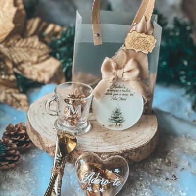Conjunto de presente natalício com saco transparente, prato branco com mensagem, chá em caneca de vidro, colheres douradas e coração transparente com texto, decoração de inverno.