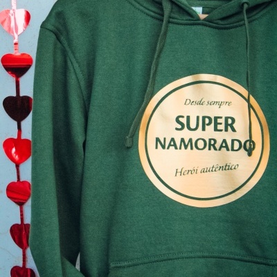 Sweatshirt verde escuro com estampado dourado e capuz pendurada num cabide de madeira