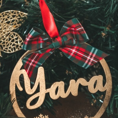 Ornamento de Natal dourado com nome Yara e laço xadrez pendurado em árvore de Natal