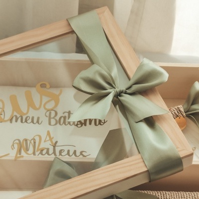 Caixa de madeira com tampa transparente e fita verde, contendo lembrança para batismo.