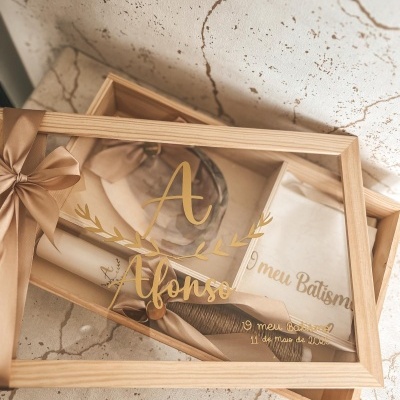 Caixa de madeira com tampa acrílica gravada a dourado, toalha bege e fita castanha com laço