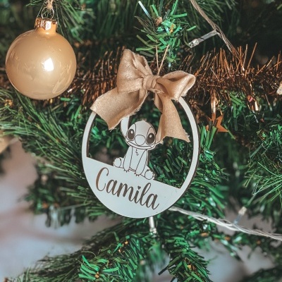 Ornamento de Natal redondo com personagem e o nome Camila pendurado num ramo de árvore de Natal verde