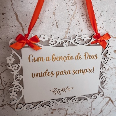 Placa decorativa branca com texto dourado e fita laranja pendurada na parede