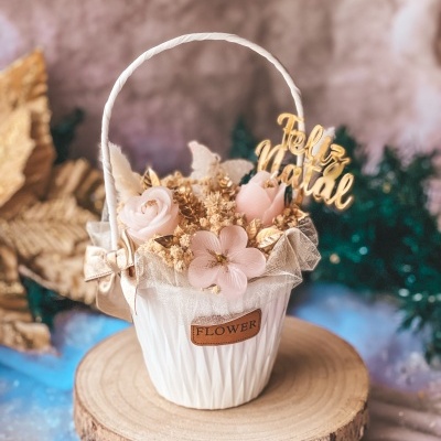 Cesto branco com flores artificiais rosa e douradas e placa Feliz Natal em fundo desfocado