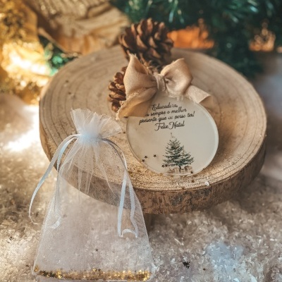 Ornamento de Natal redondo com desenho de árvore, laço dourado e pinhas sobre tronco de madeira