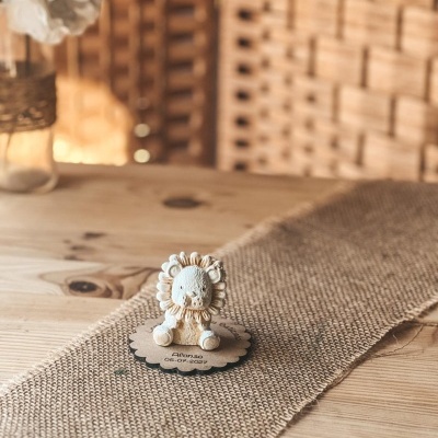 Estatueta pequena de leão creme sobre base de papel castanho com texto Afonso 06-07-2027